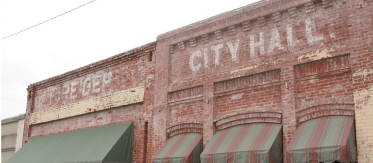 Faded "City Hall" lettering painted on the brick facade of a historic downtown building with striped awnings